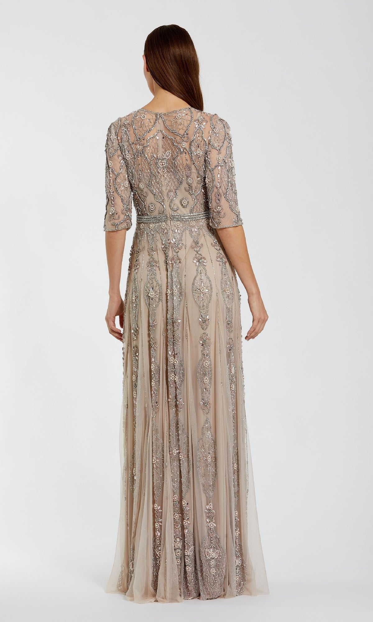 A woman stands facing away, wearing the Hand-Beaded Lilac Formal Dress Mac Duggal 10115, a floor-length gown with intricate beading and embroidery and elegant elbow-length sleeves.